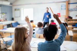 barn som räcker upp handen i klassrum